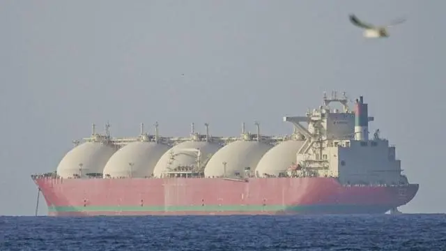 ناقلة نفط حمراء عملاقة ذات خمس قباب بيضاء ضخمة تبتعد عن الكاميرا.