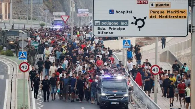 يقوم ضباط الشرطة والجنود الإسبان بمرافقة مجموعة كبيرة من المهاجرين إلى الحدود لإخراجهم من إسبانيا.