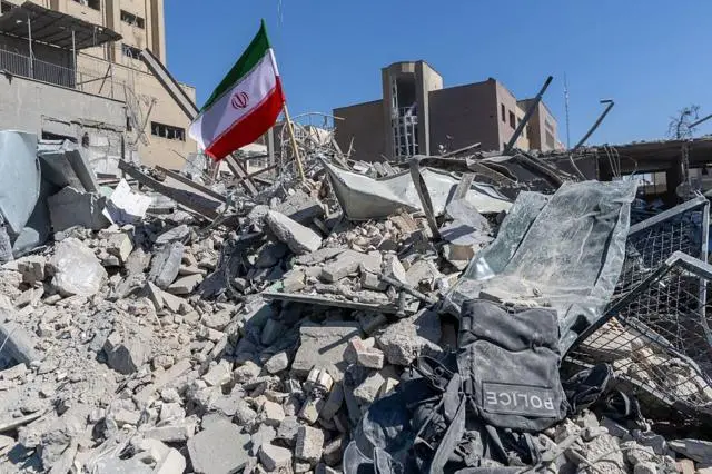 علم إيراني مغروس في أنقاض مركز للشرطة تضرر جراء غارات جوية وقعت في اليوم السابق، وذلك في 3 مارس/آذار 2026 في طهران.