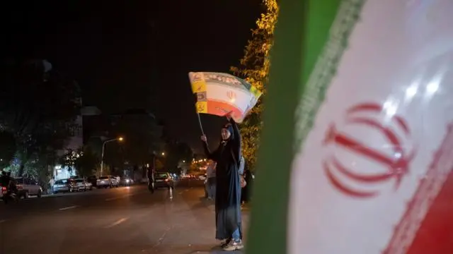 لوّحت إحدى مؤيدات الحكومة الإيرانية، وهي ترتدي النقاب، بالعلم الإيراني وهتفت بشعارات مناهضة للولايات المتحدة خلال مسيرة ليلية في وسط طهران. انتهى وقف إطلاق النار الذي استمر 60 يومًا بين إيران والولايات المتحدة في 17 أغسطس/آب، دون التوصل إلى اتفاق جديد بين الجانبين، مما أثار مخاوف من احتمال تصعيد التوترات.