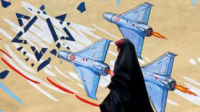 يظهر في الصورة طائرات بدون طيار وهي تحطم نجمة داود مرسومة على سور أحد المباني، بينما تمر امرأة ترتدي عباءة سوداء بجوار جدارية مناهضة لإسرائيل في طهران.