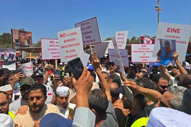 حشد من الناس، غالبيتهم رجال، يرفعون لافتات، منها لافتة كتب عليها No illegal border infiltrators in our country "لا متسللين غير شرعيين عبر الحدود في بلادنا"